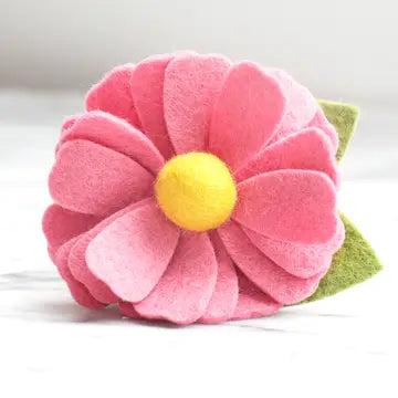 A vibrant pink felt flower accessory with a yellow center and a small green felt leaf on the side.
