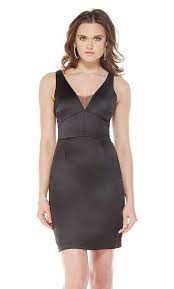 A woman wearing a sleek black satin cocktail dress with a V-neckline, sheer mesh inset, and a fitted silhouette, posing against a white background.