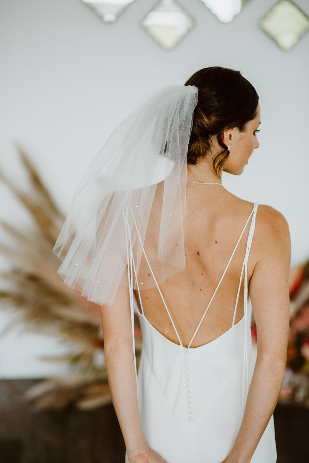A bride from the back wearing a shoulder-length sheer white tulle veil with delicate pearl accents