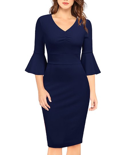 A woman in a navy blue, knee-length bodycon dress with a V-neckline, gathered bust detail, and three-quarter bell sleeves.