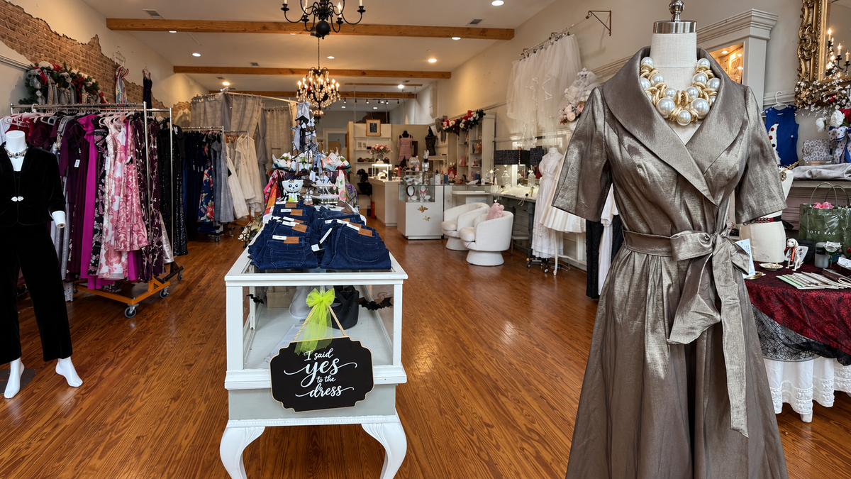 Metallic taupe wrap dress with a tie belt and statement pearl necklace on a mannequin inside a boutique