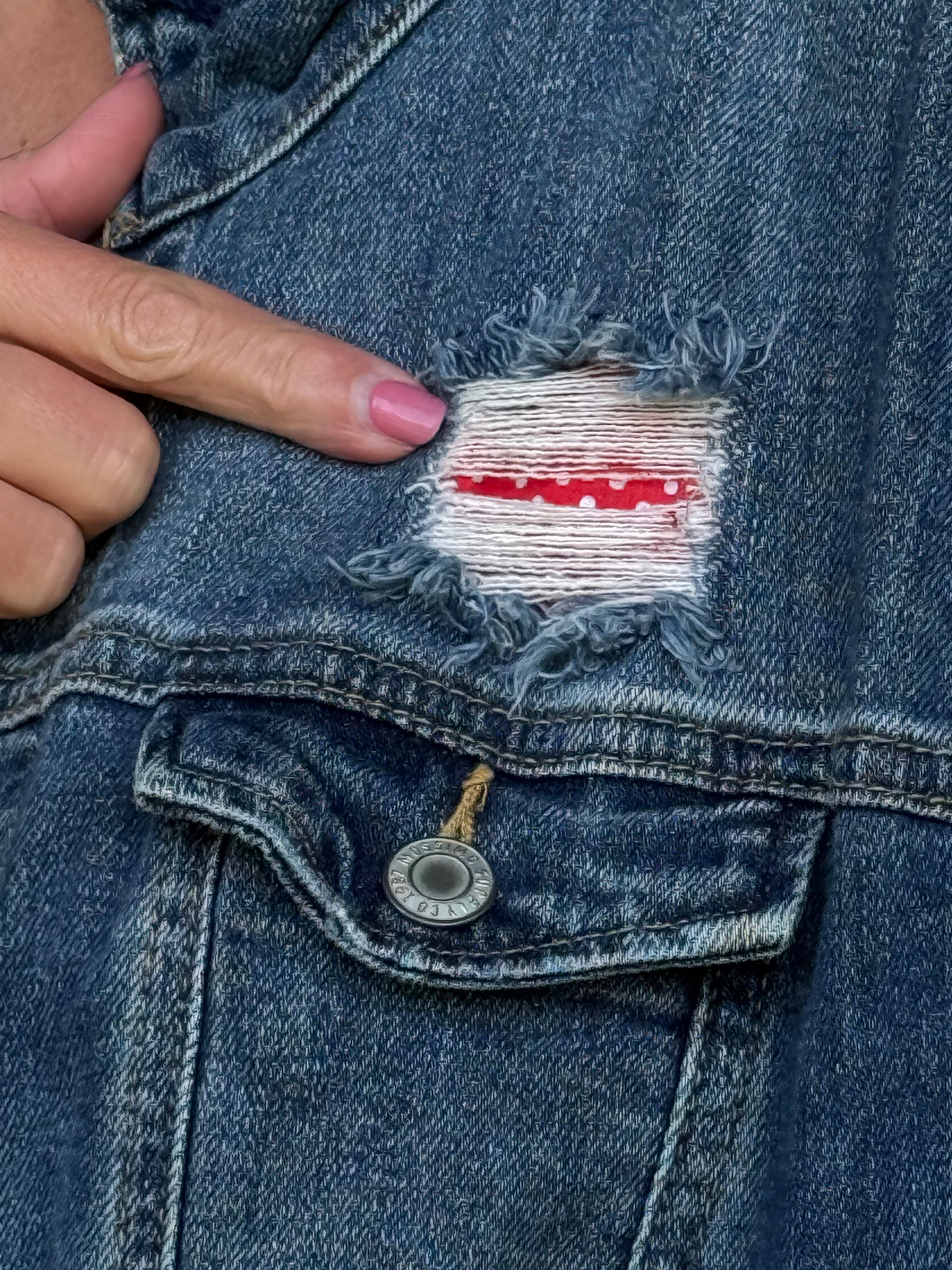 Close-up of the distressed front of an upcycled denim jacket showing red and white flag fabric and a Mossimo button at Dover Grace Boutique in Watkinsville, Georgia.