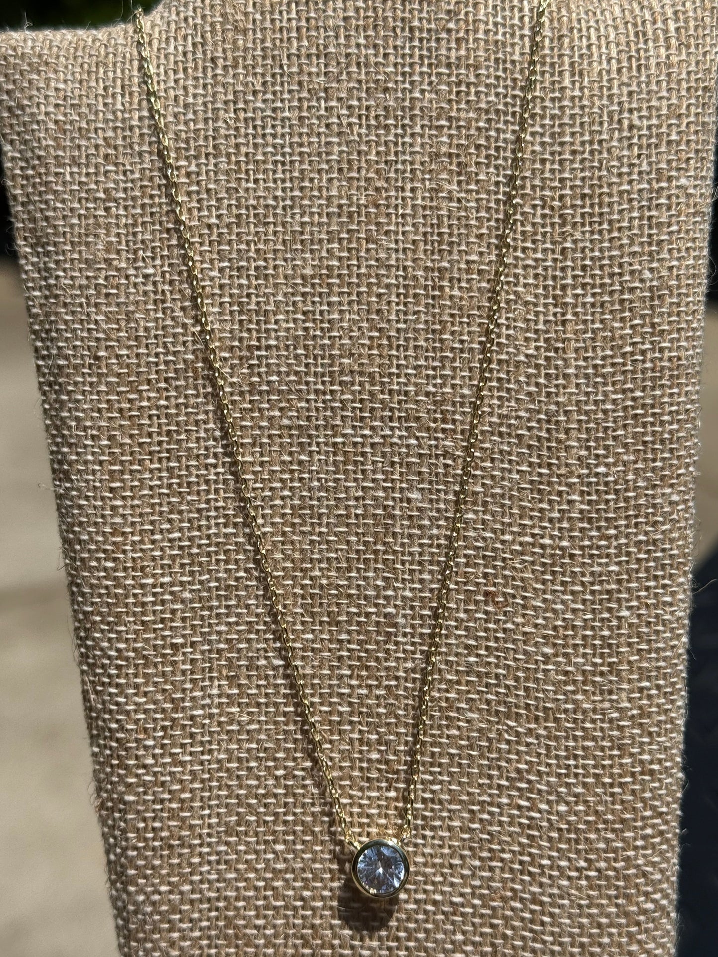 Dainty gold-tone necklace featuring a single crystal stone in a bezel setting, layering jewelry