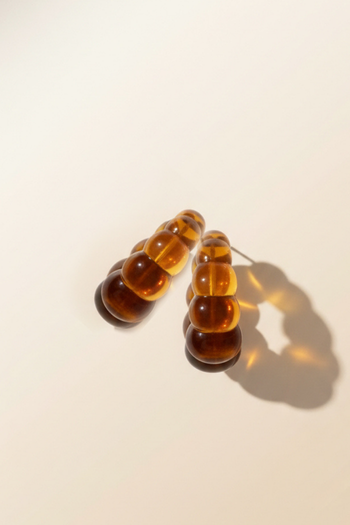 A pair of amber-colored, translucent resin hoop earrings with a tiered, bubbled texture