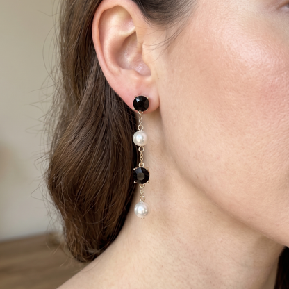 Gold-tone earrings with alternating black crystal and white pearl drops in a vertical cascade.