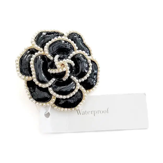 A glossy black flower brooch featuring a layered Camellia-style design, outlined with delicate white seed pearls and attached to a white tag labeled "Waterproof."