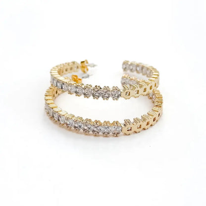 A pair of gold hoop earrings lined with clear, square-cut stones on a white background.
