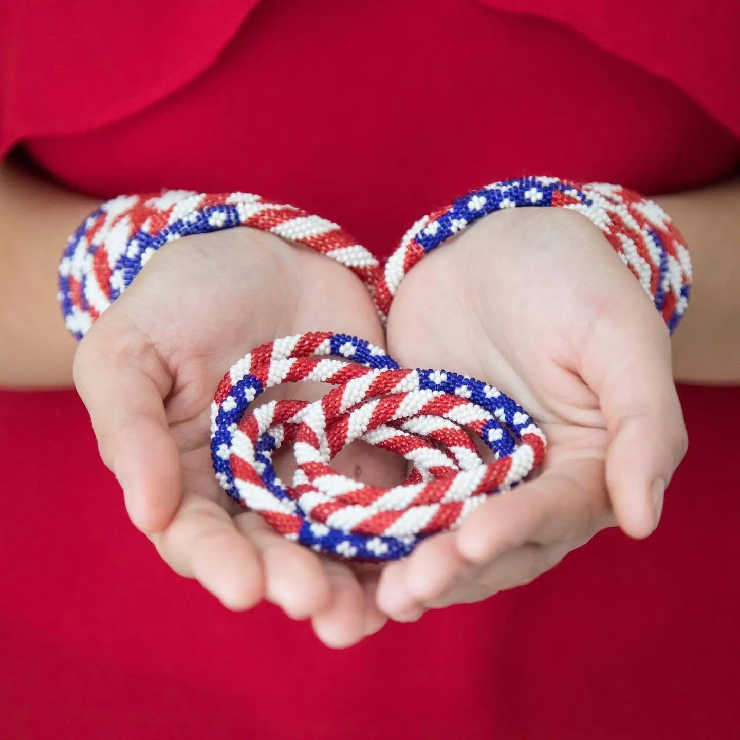 Red, white, and blue braided bracelets on a person's hands against a red background