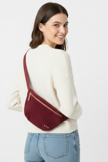 A burgundy woven fanny pack with a soft, velvet-like texture, featuring a gold-tone zipper, three small gold studs, and a matching adjustable strap.