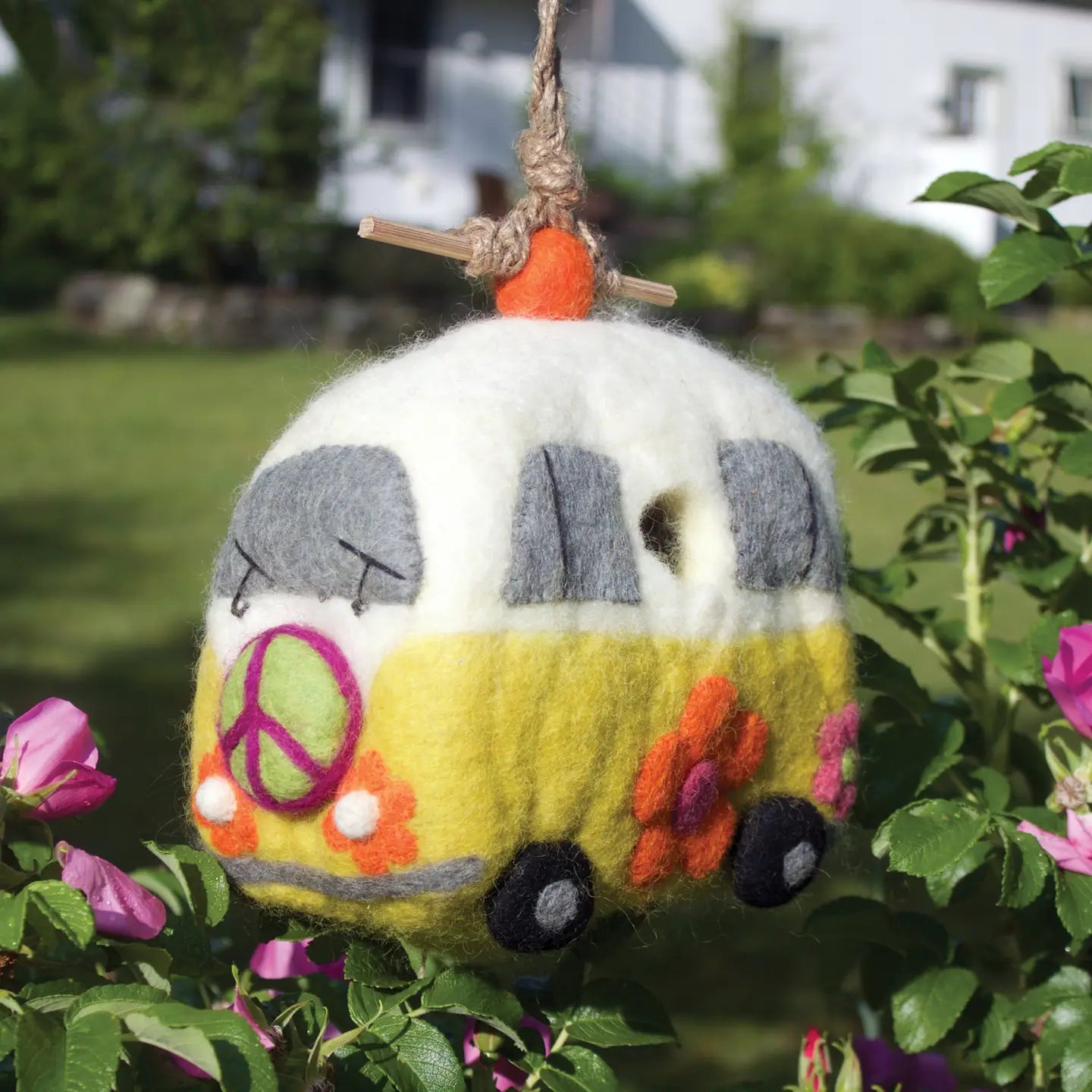 A yellow and white felt birdhouse shaped like a retro bus with a green peace sign and orange flowers.