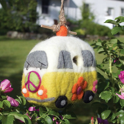 A yellow and white felt birdhouse shaped like a retro bus with a green peace sign and orange flowers.