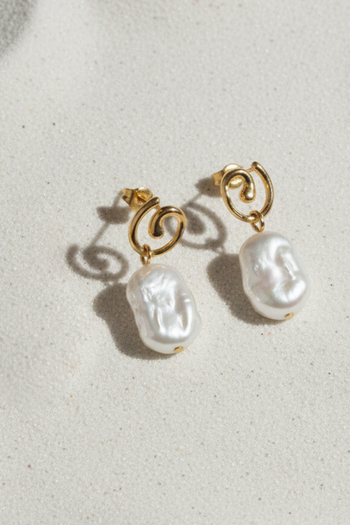 a gold swirl earring featuring a large, irregular baroque pearl drop.
