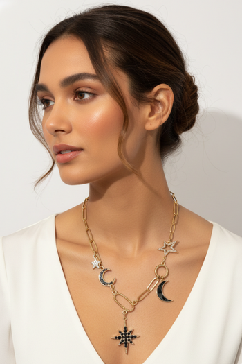 Gold celestial charm necklace featuring a mix of textured paperclip links and various charms, including a large black starburst pendant, crystal-encrusted moon and star charms, and a solid black crescent moon.