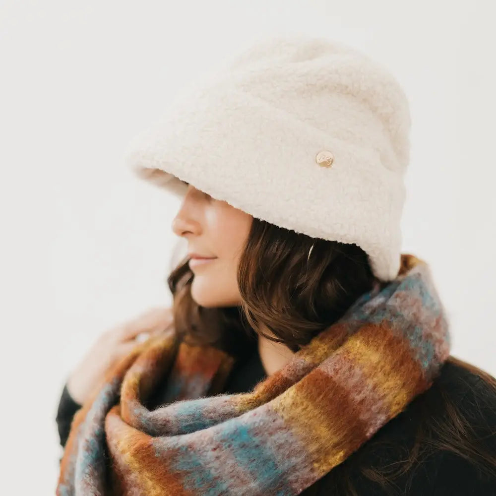 Person wearing a white knit hat and colorful scarf on a light background