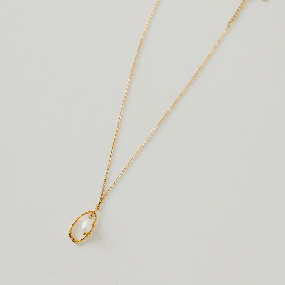 A gold chain necklace with a textured open oval pendant featuring a single white pearl on a white background.