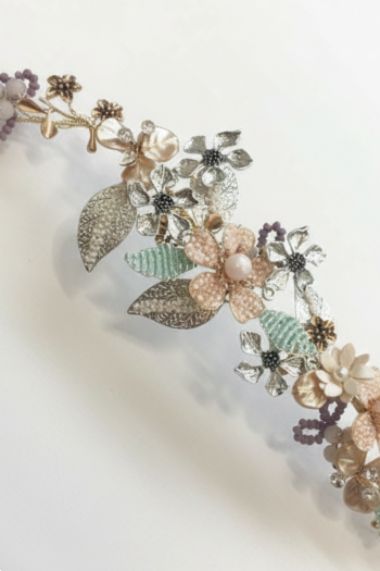 An intricate bridal hair vine decorated with blush-colored flowers, light green leaves, and purple beaded accents.