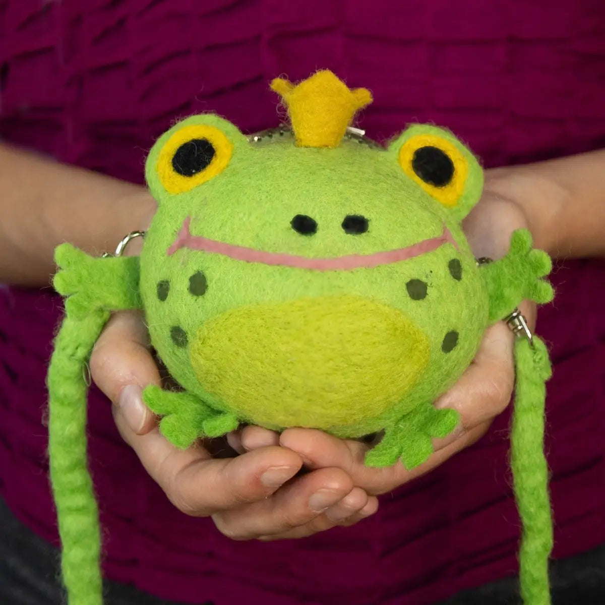 A green felt purse shaped like a frog wearing a yellow crown with a shoulder strap.