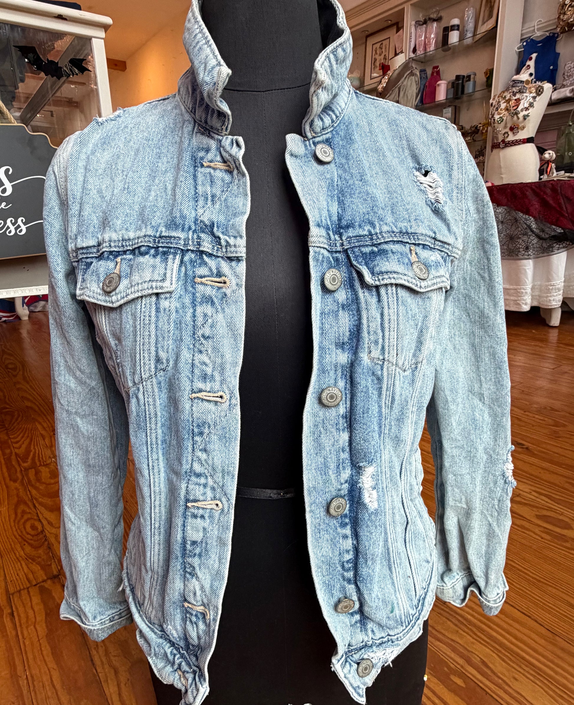 Front of a light wash distressed denim jacket with metal buttons and flap chest pockets.