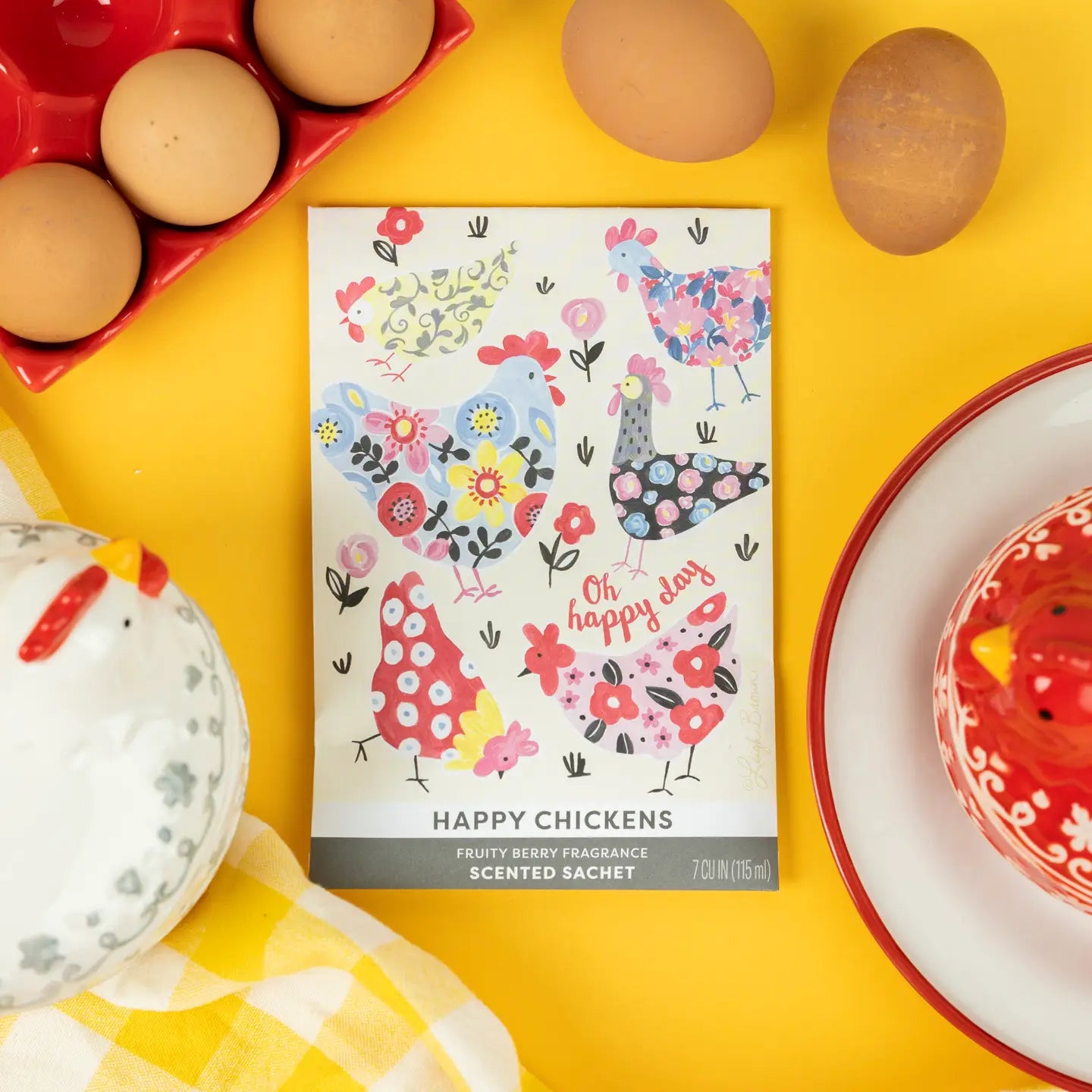 Happy Chickens scented sachet on a yellow background with eggs and ceramic items.