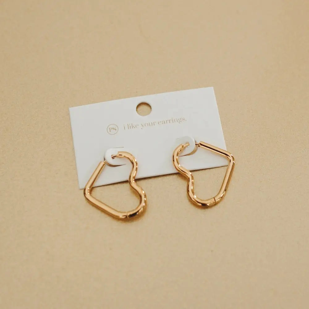 Small gold-tone heart-shaped huggie hoop earrings on a white display card.