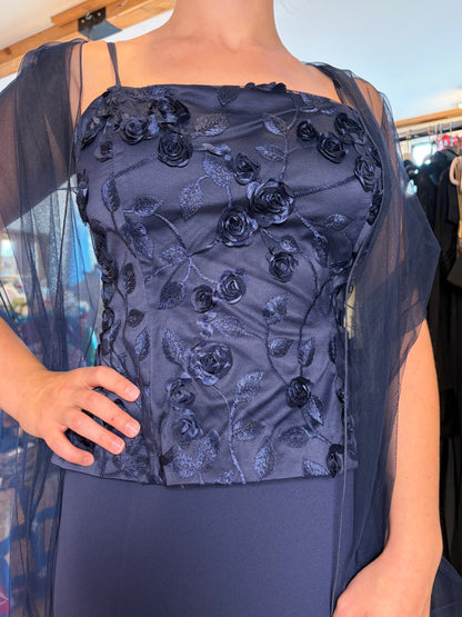 A navy blue off-the-shoulder dress featuring a structured bodice with 3D floral embroidery and a sheer mesh overlay, shown on a model.