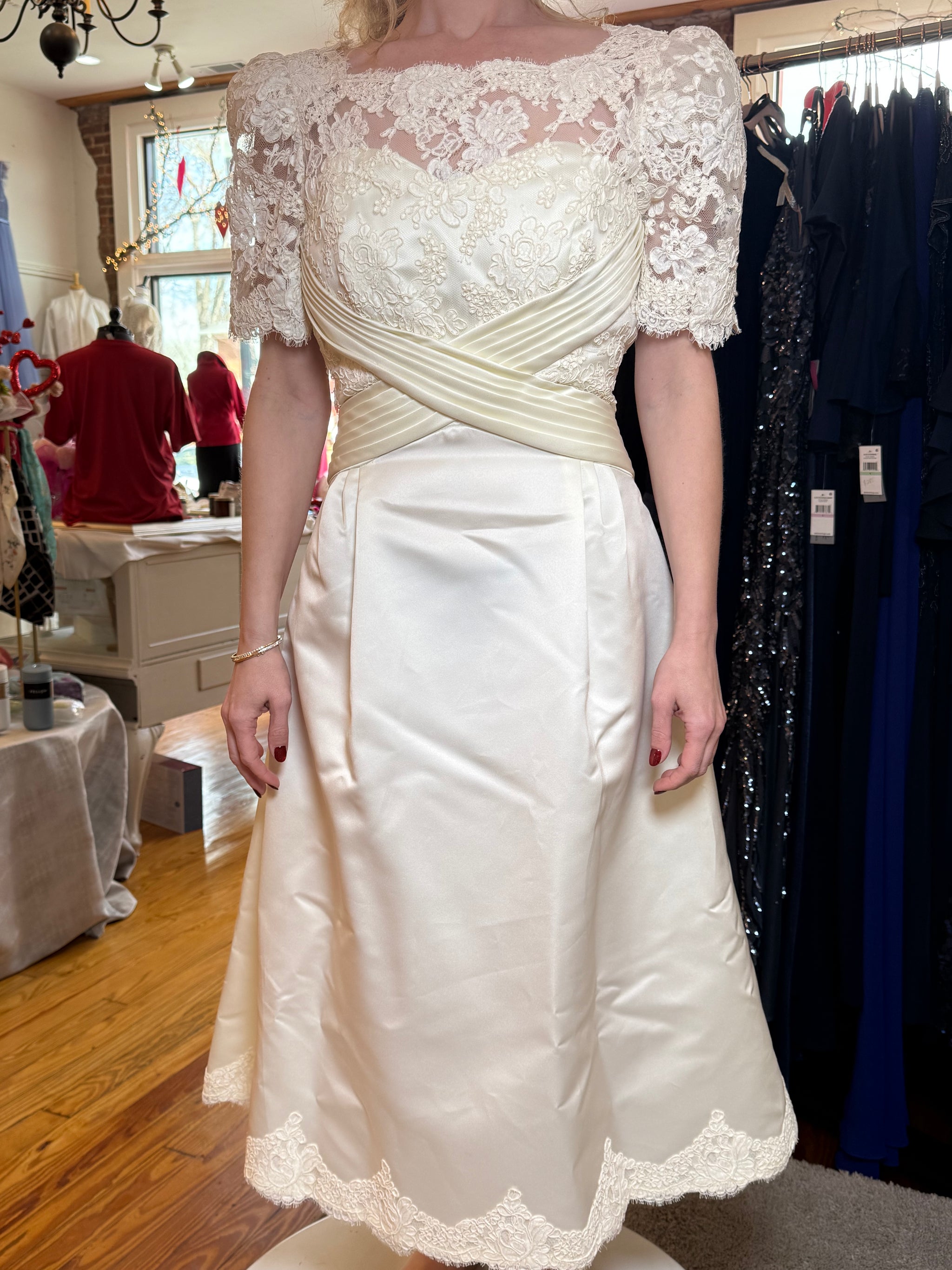 White lace dress on a mannequin in a store setting with other clothing in the background.