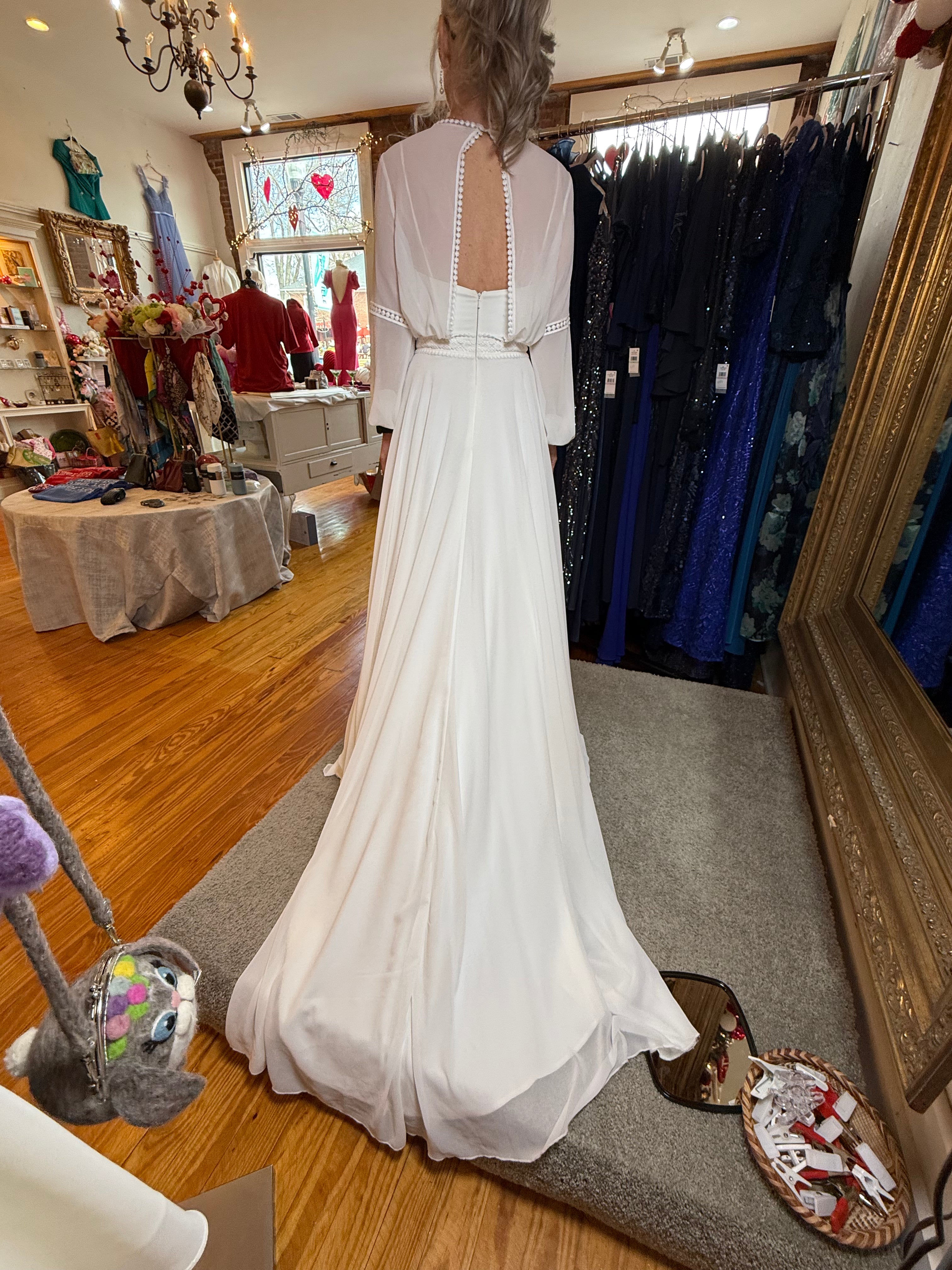 Person wearing a white dress in a store with racks of clothes and a mirror.