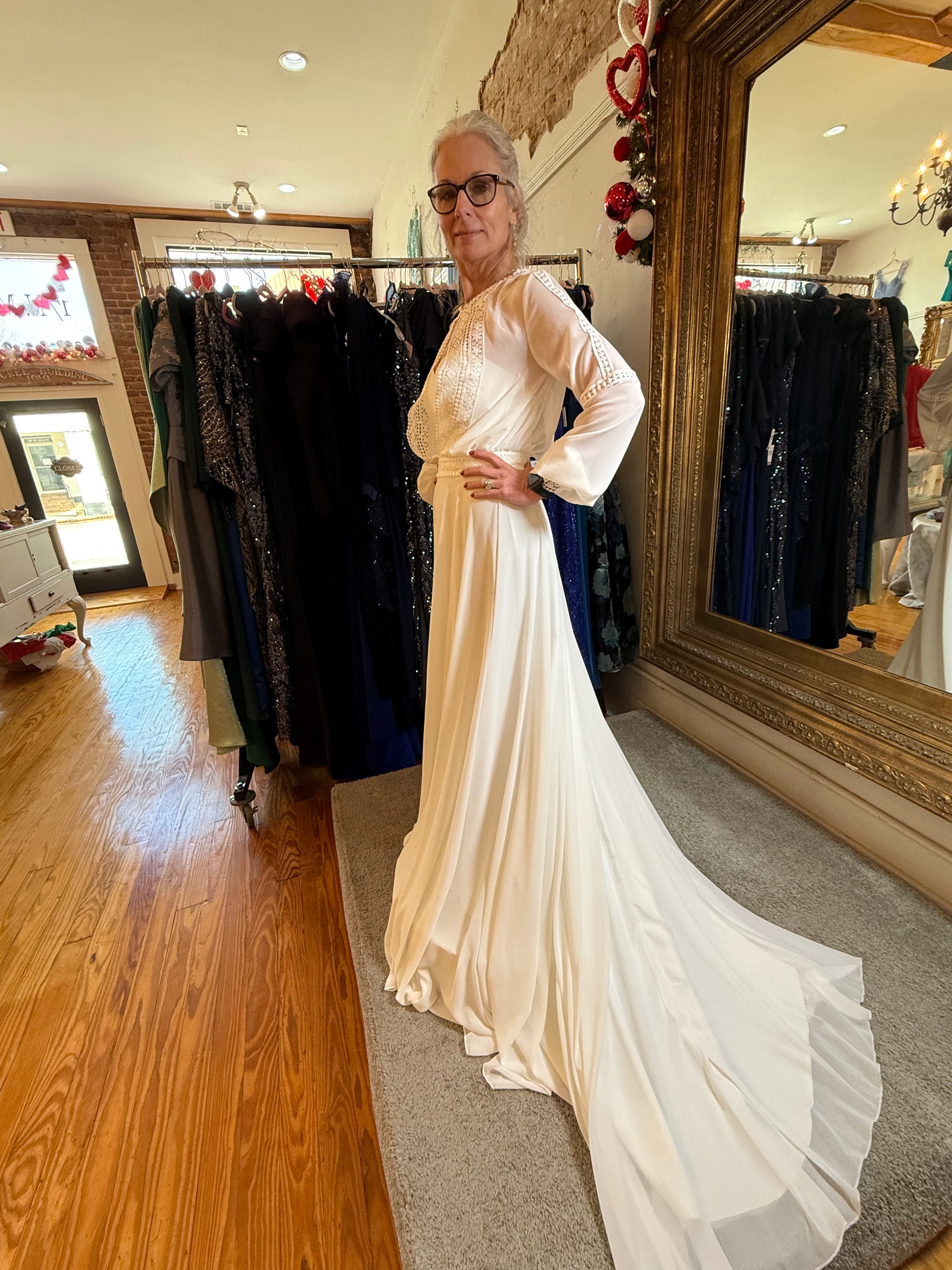 Woman in a white dress standing in a clothing store with a large mirror.