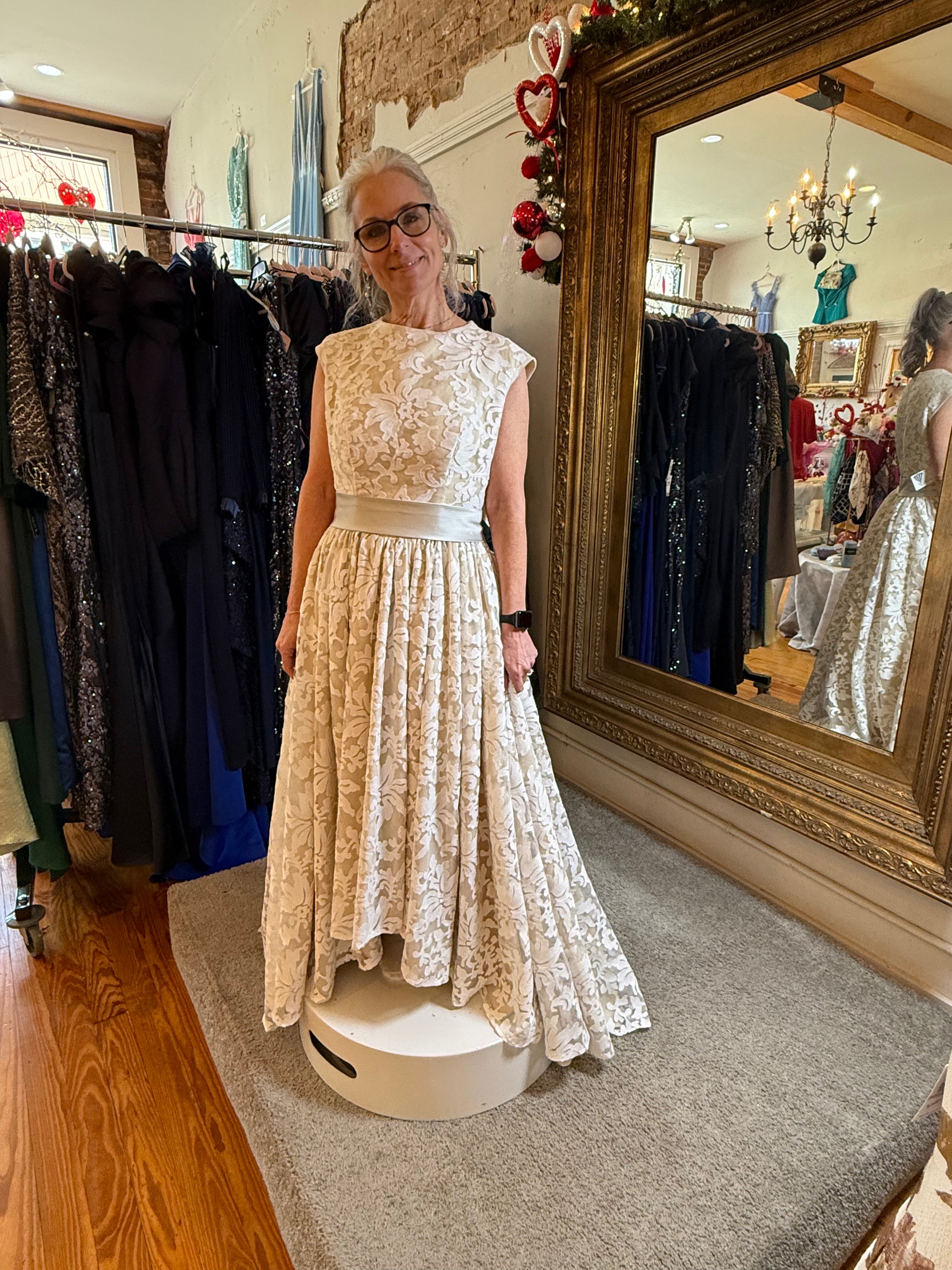 Woman in a lace dress standing in a clothing store with a large mirror.