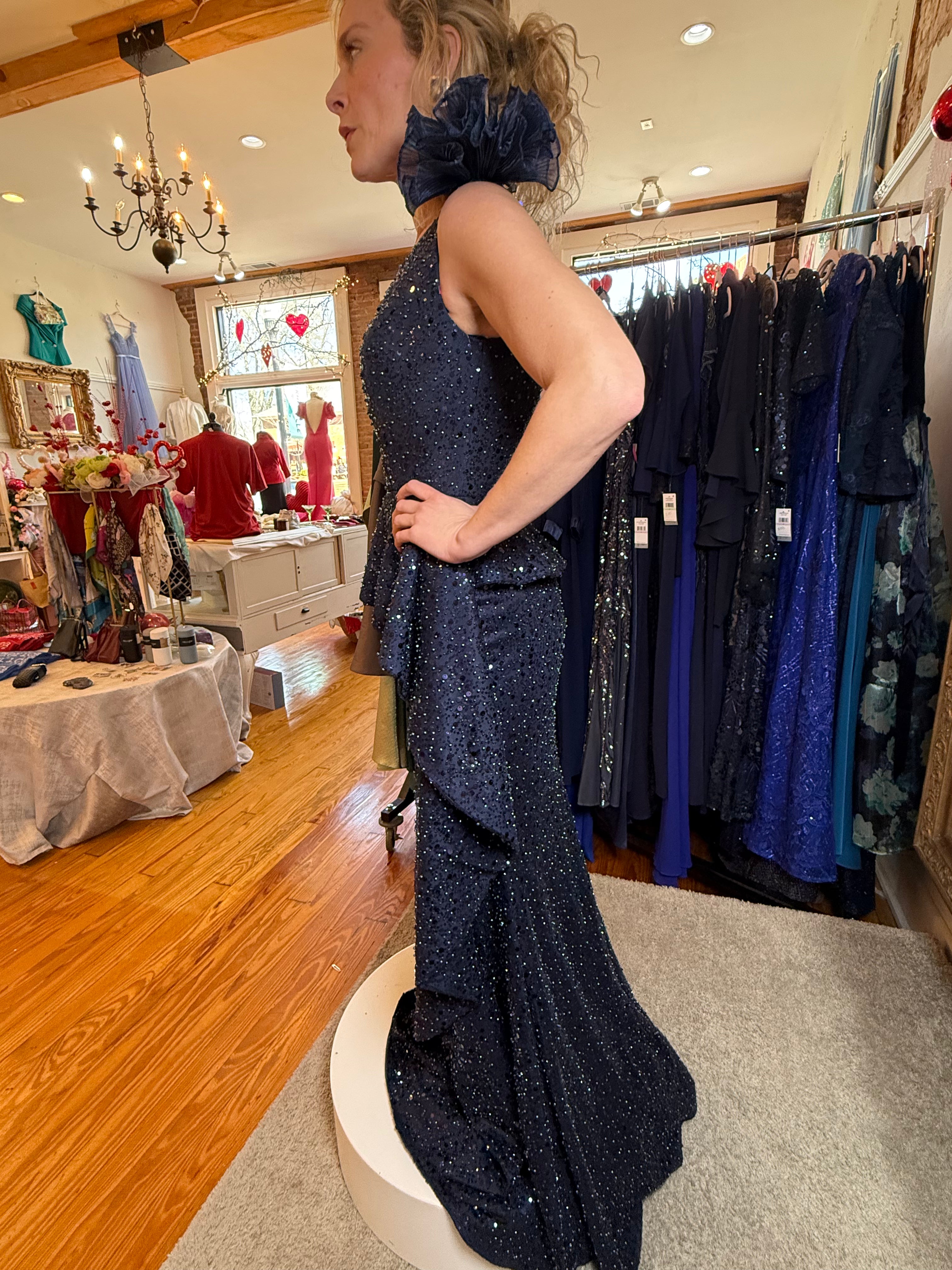 Woman in a sparkly blue dress standing in a clothing store with racks of dresses in the background.