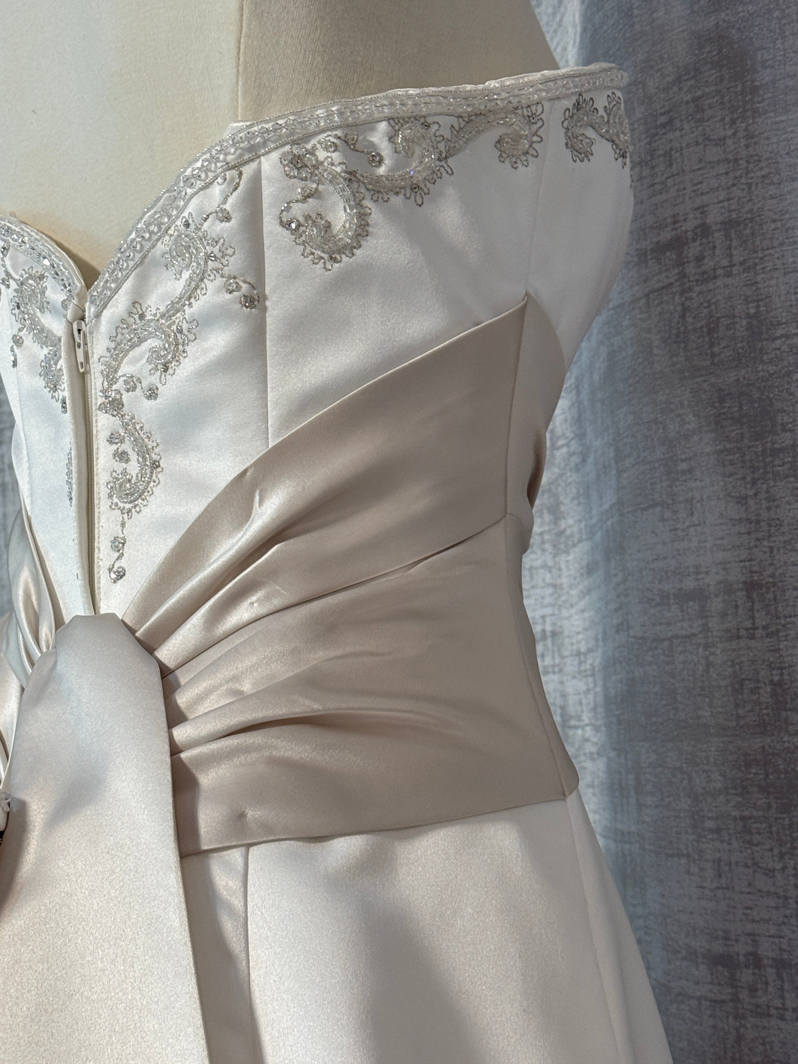 Detail view of contrast champagne satin ruched waist sash on ivory Mon Cheri wedding gown, showing pleated fabric gather and silver beaded bodice above