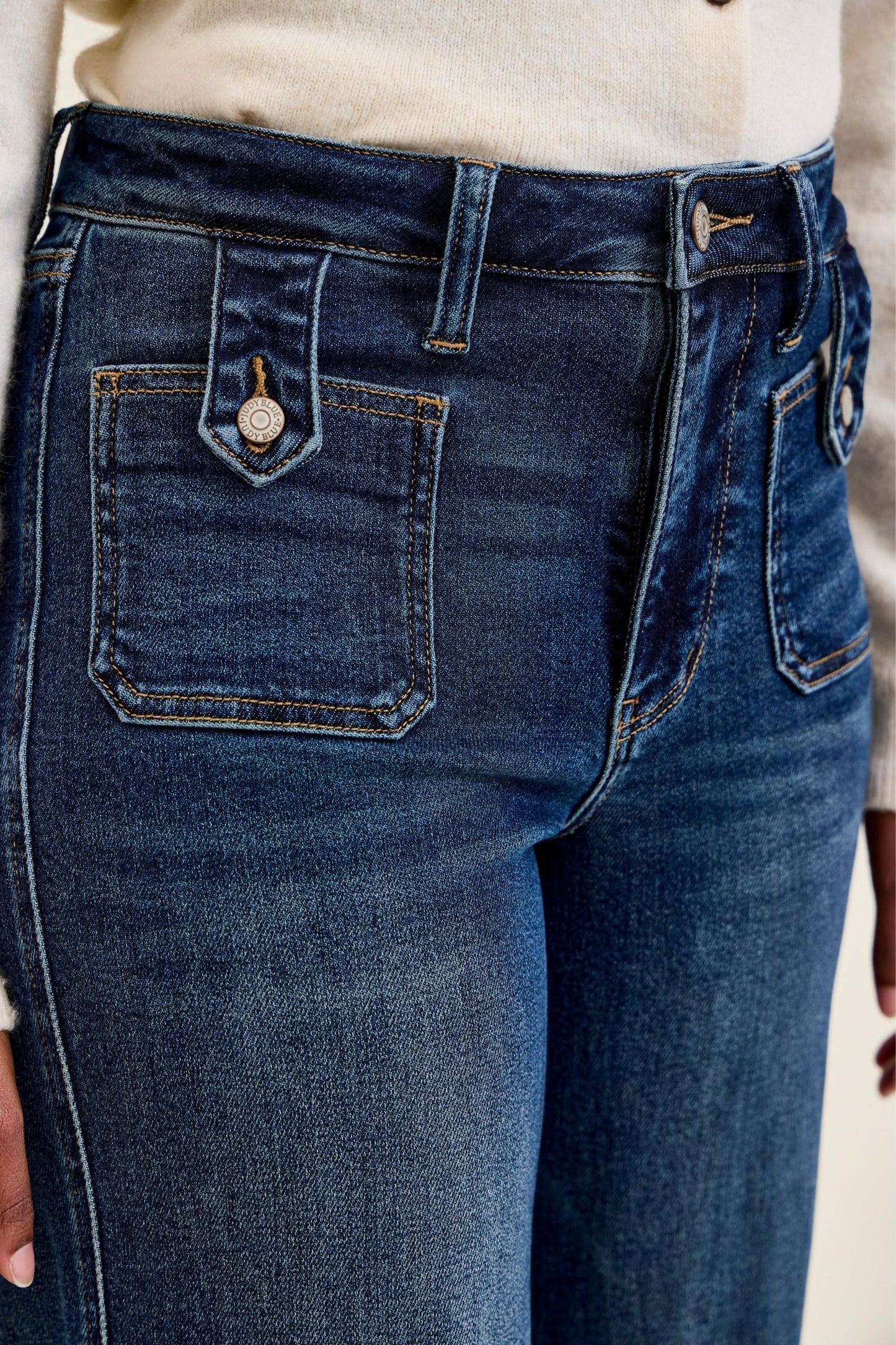 Close-up of Judy Blue Retro Wide Leg jeans showing front patch pocket with branded tab button closure, high waist waistband, and dark fade indigo denim with contrast stitching