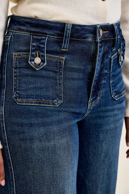 Close-up of Judy Blue Retro Wide Leg jeans showing front patch pocket with branded tab button closure, high waist waistband, and dark fade indigo denim with contrast stitching