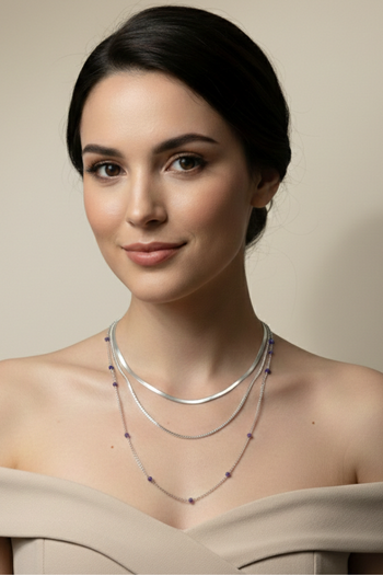 A silver-toned three-strand layered necklace set featuring a flat herringbone chain, a classic link chain, and a delicate beaded chain with small purple accents.
