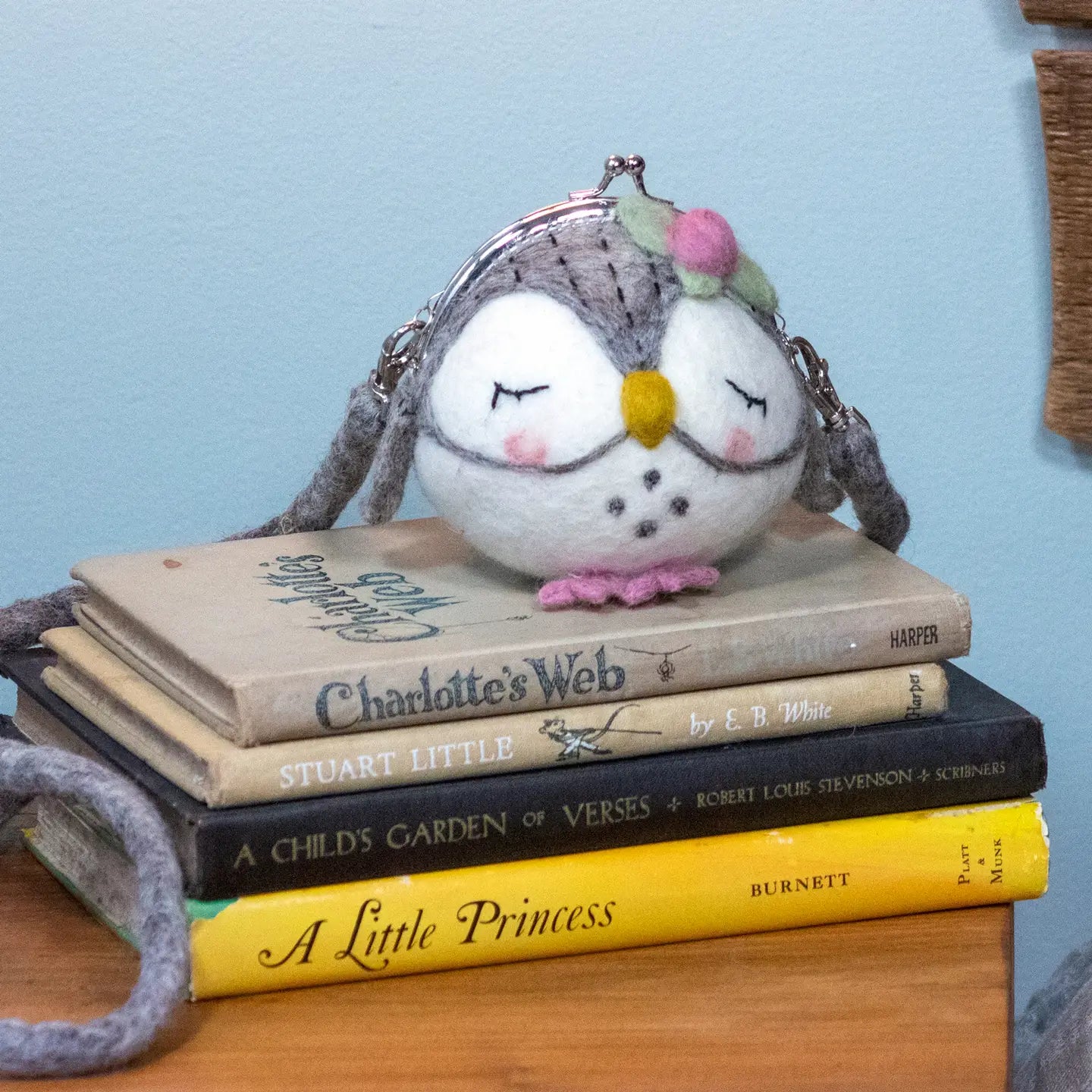 A round, grey and white felt purse shaped like a sleeping owl with a shoulder strap.