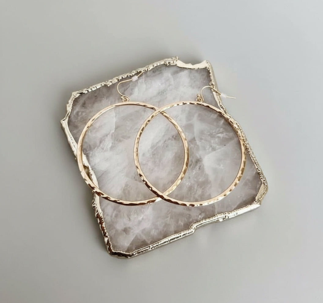 Pair of 2.5-inch textured gold hoop earrings with a hammered finish on a light gray background.