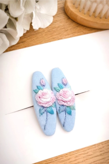 Pair of light blue hair clips with floral designs on a white surface.