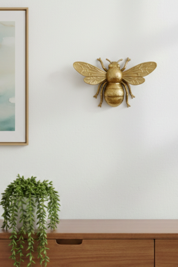 A small, metallic gold honeybee wall hanging with detailed wings