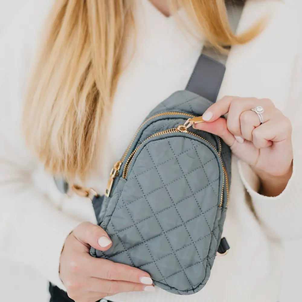 Person holding a gray quilted waist bag with gold zippers.