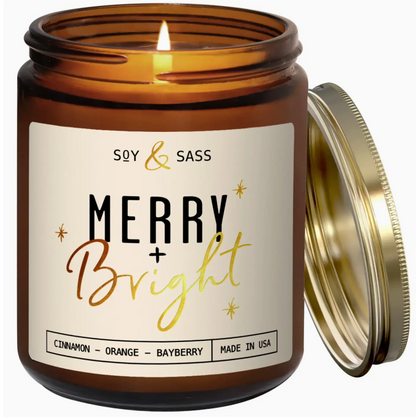 Candle jar with 'Soy & Sass' label featuring 'Merry + Bright' text, open lid on a white background.