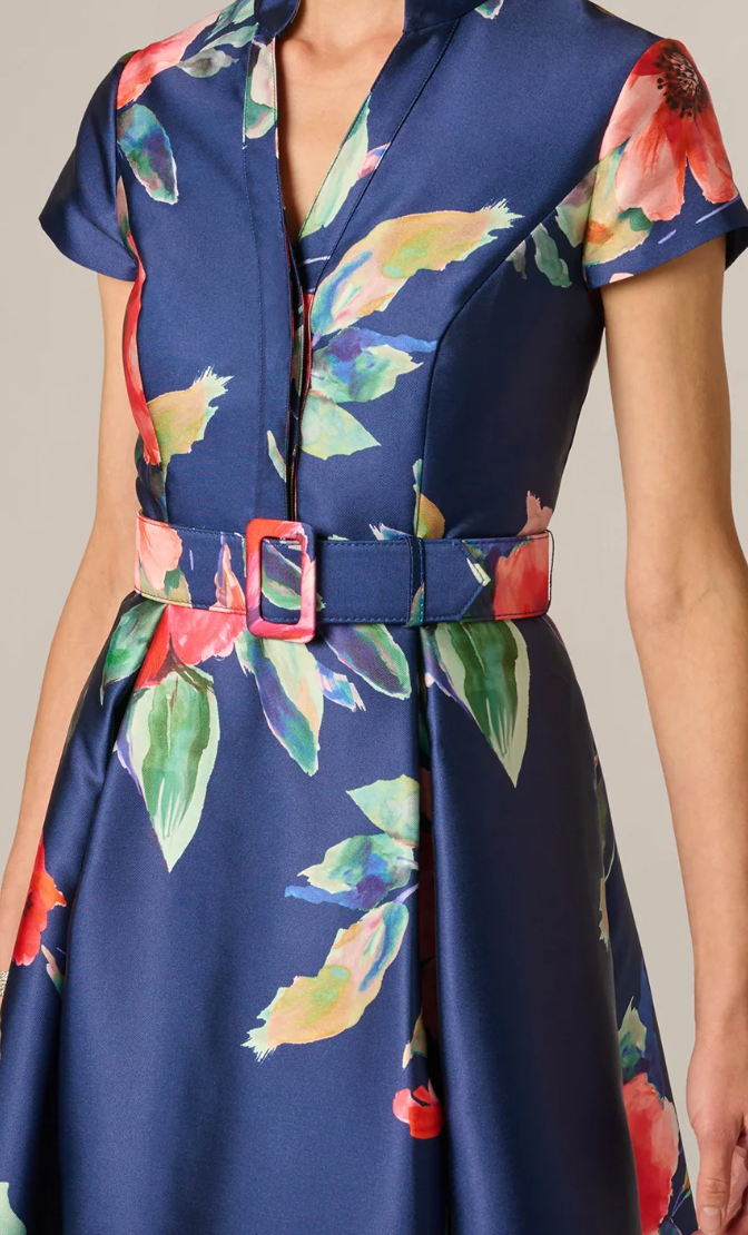 A close-up of a woman wearing a navy blue satin dress with a vibrant multicolor floral print and a matching belt with a red buckle.