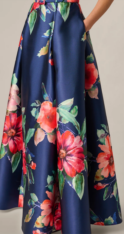A close-up of a navy blue satin skirt with a large watercolor floral print in red, pink, and green, shown on a model against a neutral beige background.