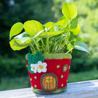 A red felt pot shaped like a strawberry house with a yellow door and white flowers on a white background.
