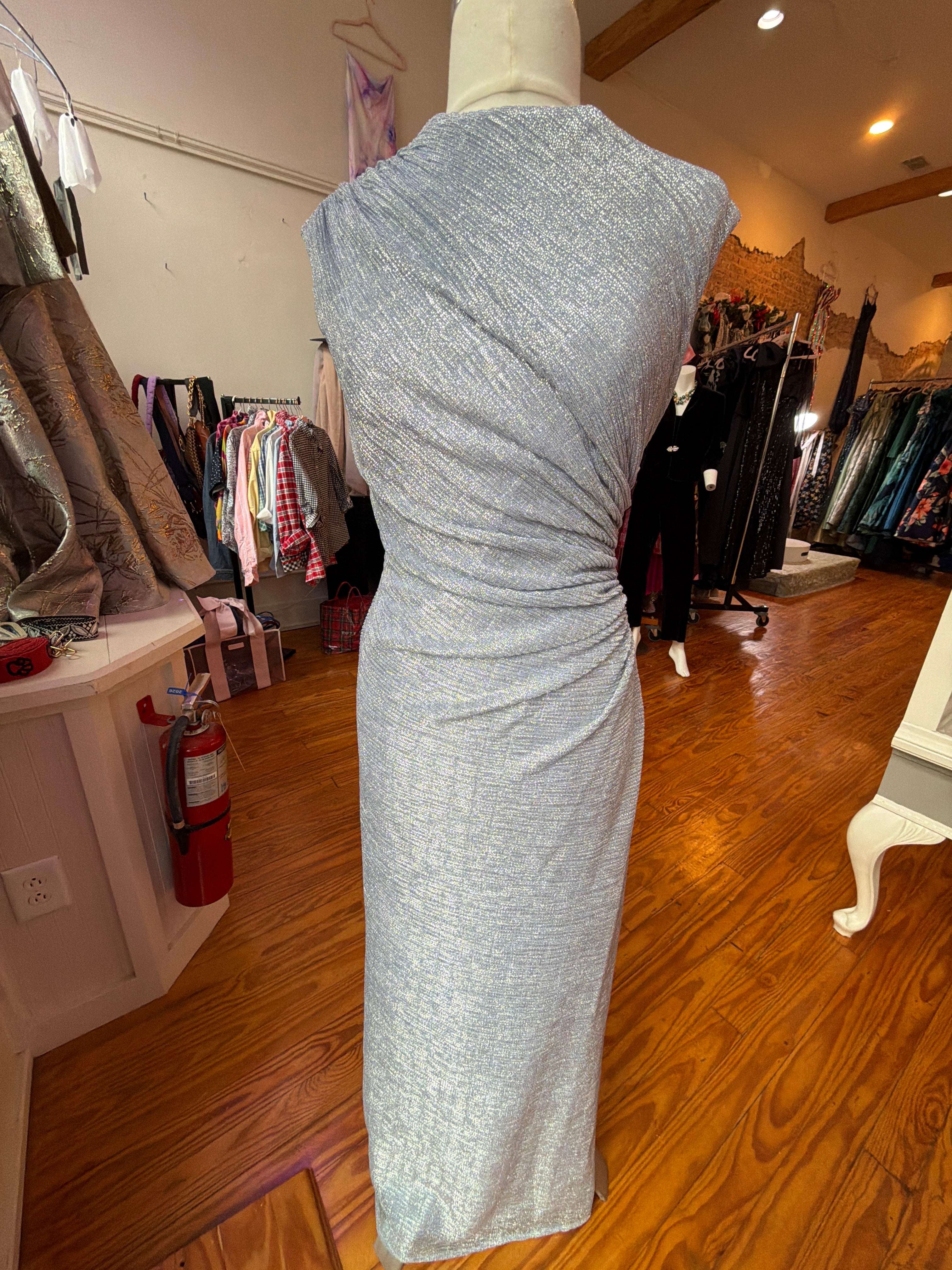 Periwinkle metallic gown with a ruched waist on a mannequin beside clothing racks in the boutique.