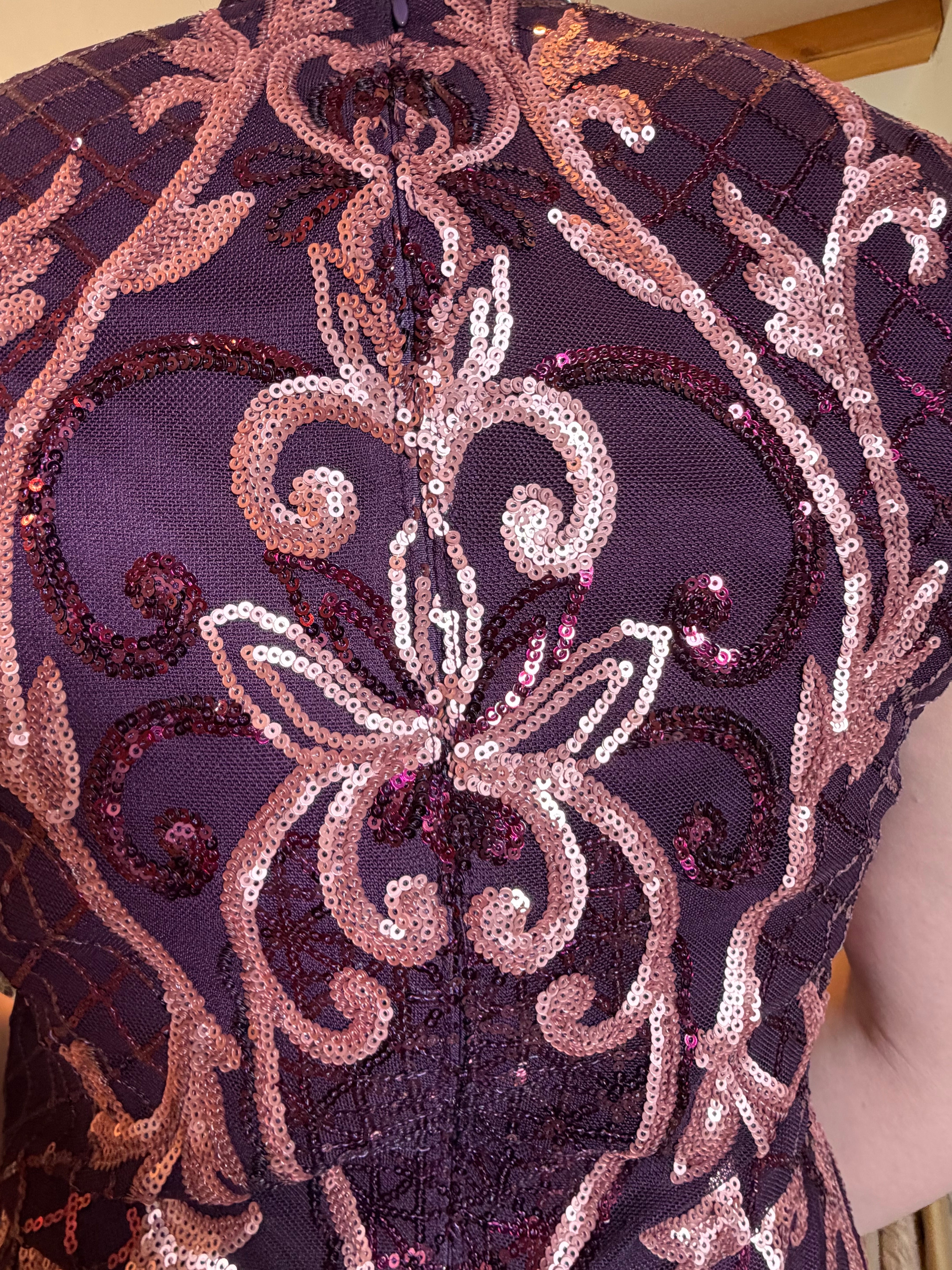 Close-up of rose scroll embroidery and sequins on wine-colored gown fabric.
