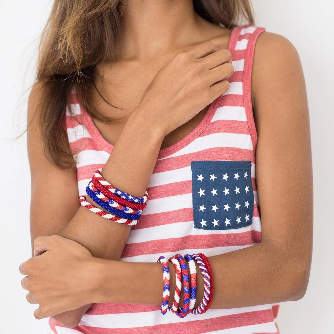 A woman wearing stacks of red, white, and blue beaded spiral bracelets on both wrists.