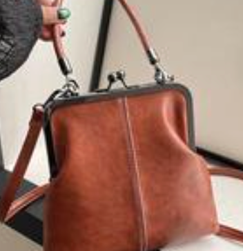 Vintage brown women’s satchel handbag with structured frame, top handle, and adjustable shoulder strap displayed indoors.