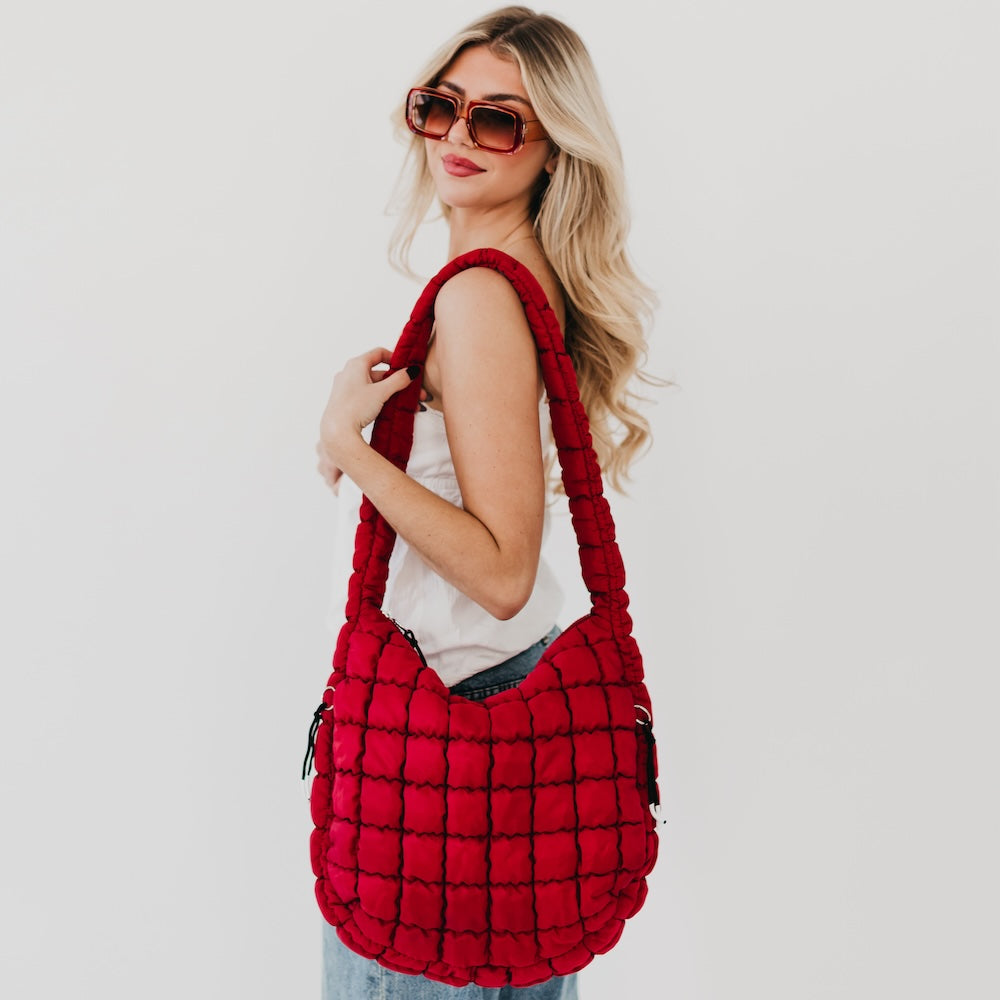 A vibrant red quilted hobo bag featuring a large puffer-style square pattern and thick matching shoulder straps.