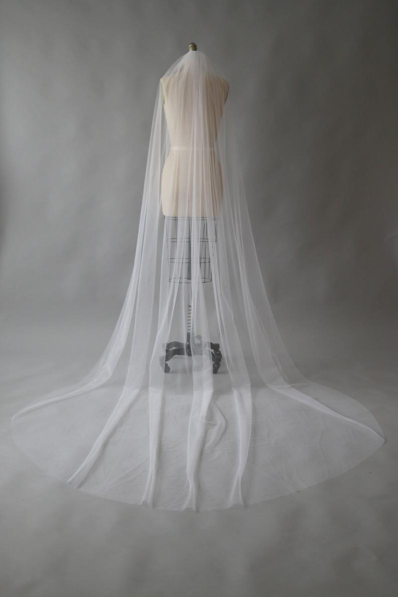 A cathedral-length wedding veil in sheer white tulle draped over a dress form and pooling on the floor.