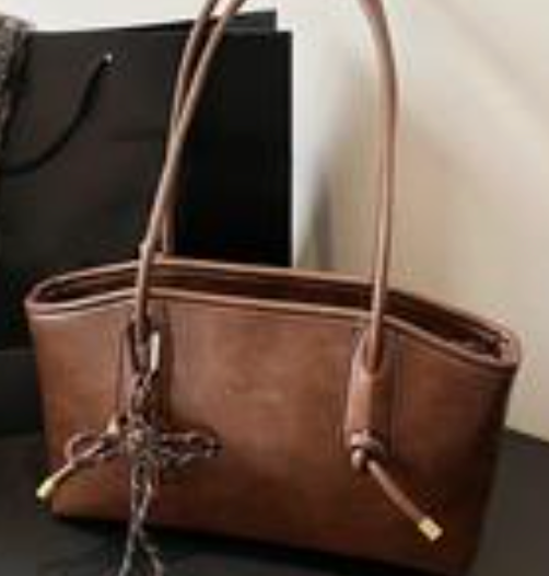 Brown minimalist women’s shoulder tote bag with long straps and large capacity design displayed on a dark surface.